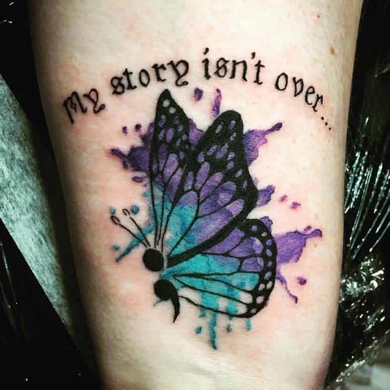 A purple and blue watercolor butterfly tattoo with a semicolon body and the phrase 'My story isn't over,' symbolizing hope and perseverance