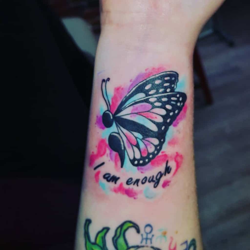 A semicolon butterfly tattoo with pink accents and the phrase 'I am enough,' symbolizing self-acceptance and mental health awareness