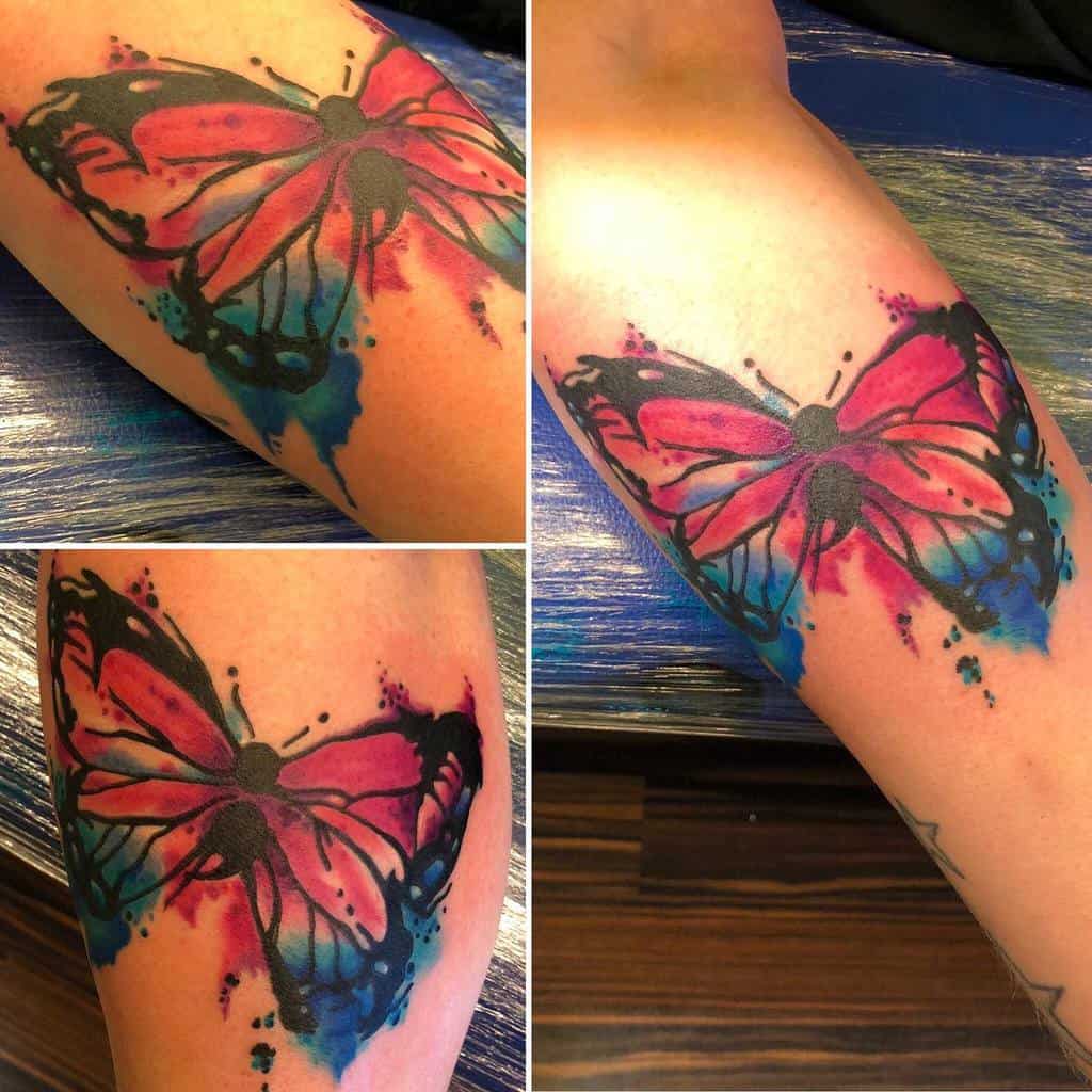 A bold watercolor butterfly tattoo with pink and blue splashes and a semicolon body, representing strength and mental health awareness