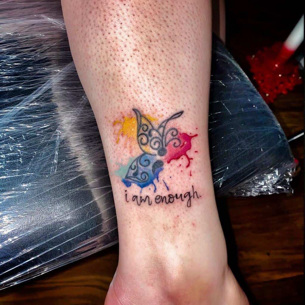 A small semicolon butterfly tattoo with colorful splashes and the phrase 'I am enough,' symbolizing self-worth and mental health awareness