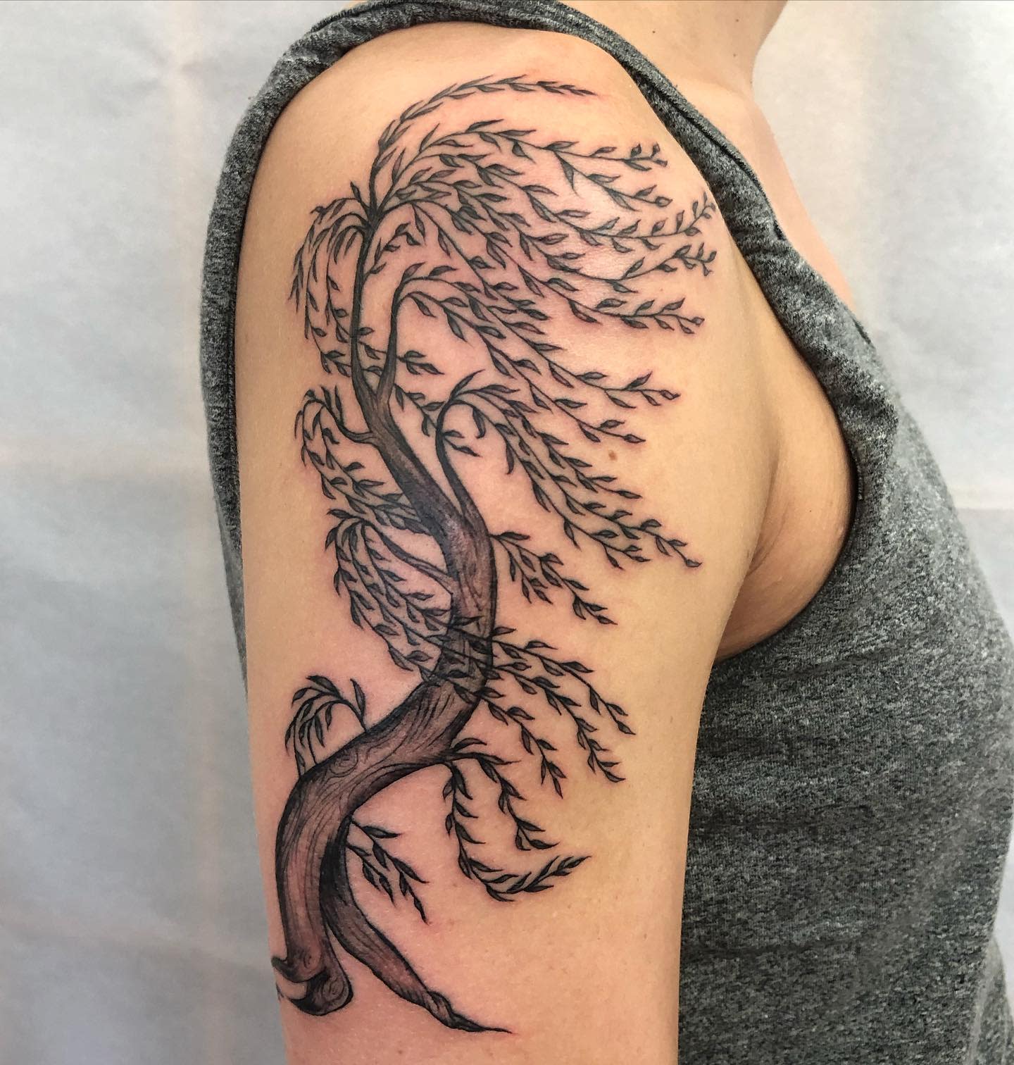 Tattoo of a willow tree on an upper arm with the branches flowing in the wind