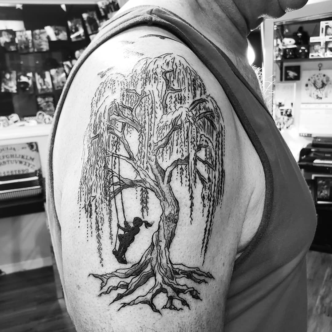 Black and white tattoo of a willow tree with a swing on the upper arm