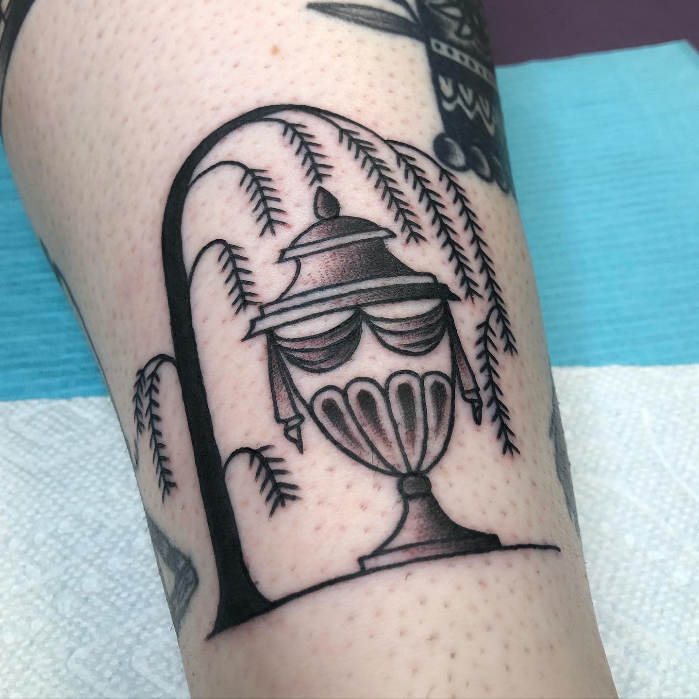 Tattoo of an ornate urn under a weeping willow tree on an arm