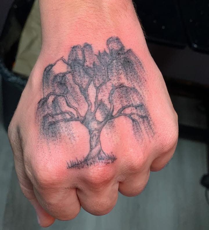 Hand with a willow tree tattoo depicting a detailed, leafless tree with shading