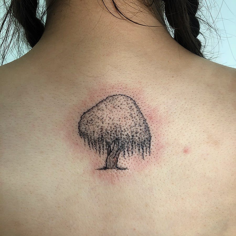 Close-up of a back with a small tree tattoo on the upper back