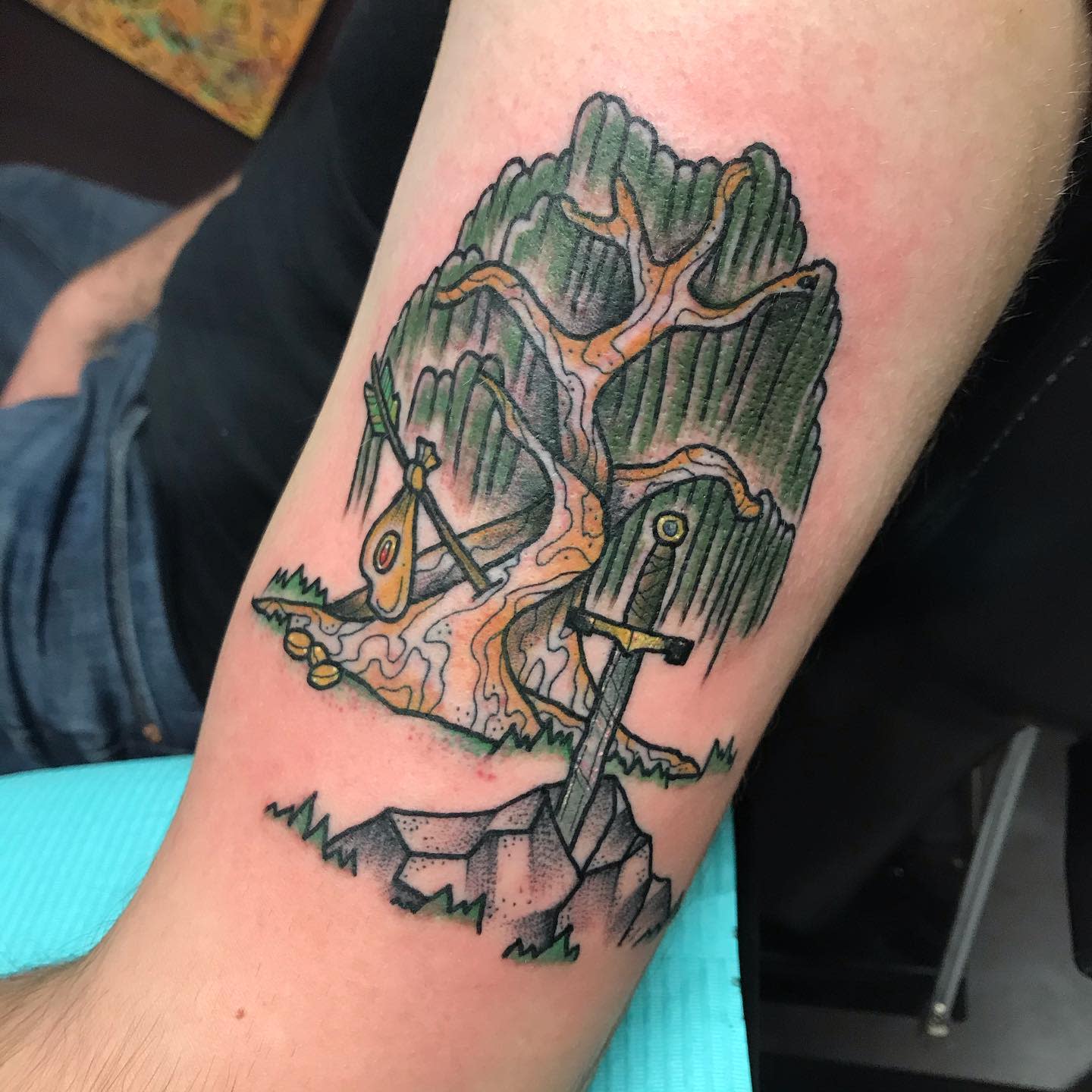 Tattoo of a tree with swords and an eye embedded in the branches on an arm