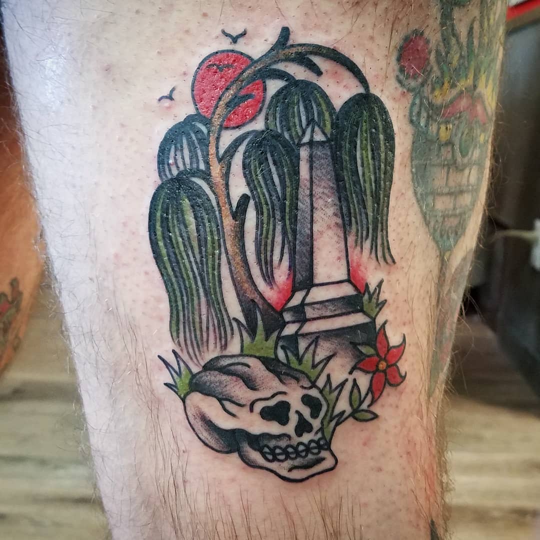Tattoo of grave with willow tree, skull, and red sun on someone's leg