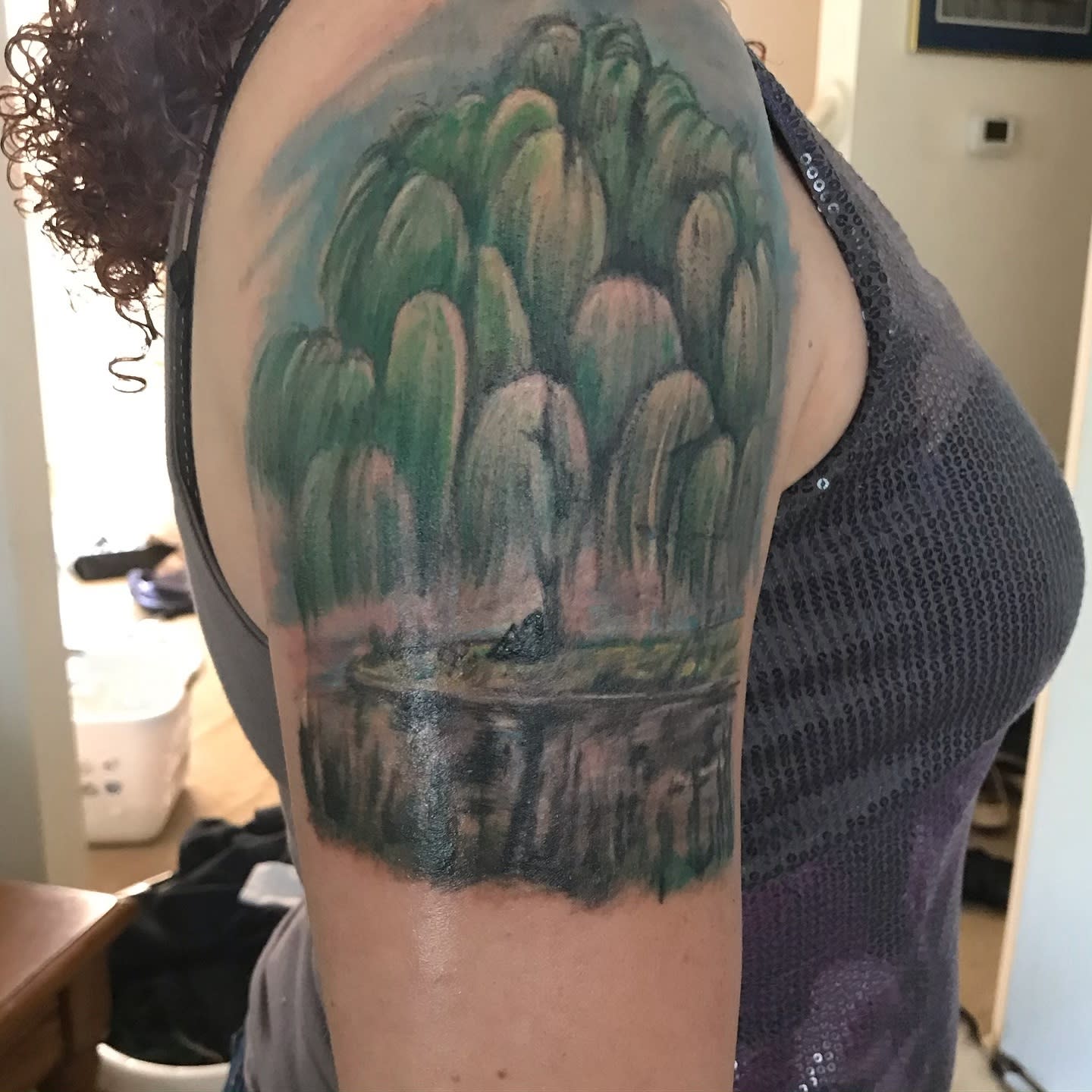 Arm tattoo depicting a serene forest scene with willows and a pond