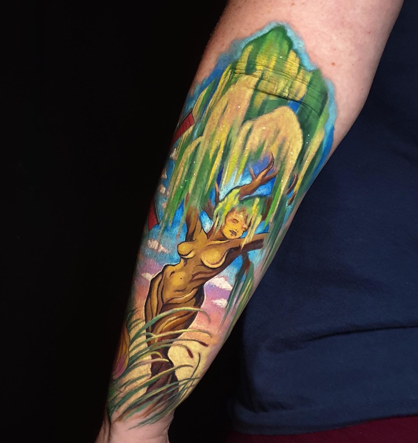 Colorful tattoo of a woman merging with a willow tree on a forearm