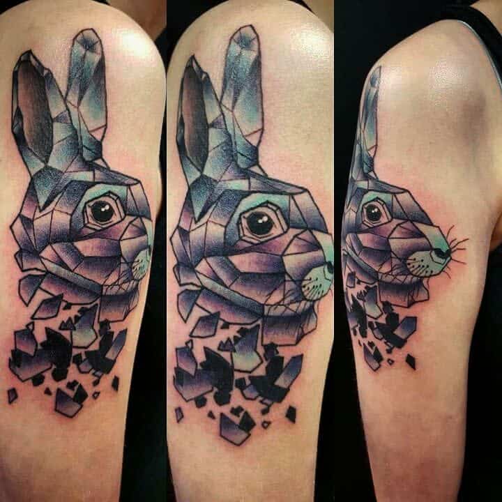 A colorful, geometric tattoo of the White Rabbit from Alice in Wonderland, with shattered fragments creating a dynamic effect