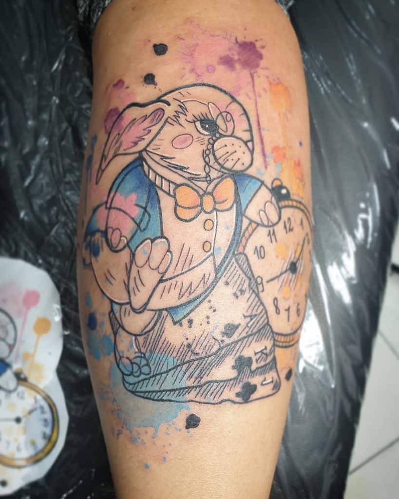 Tattoo of the White Rabbit wearing Alice's outfit from Alice in Wonderland, featuring colorful splashes, playing cards and a pocket watch