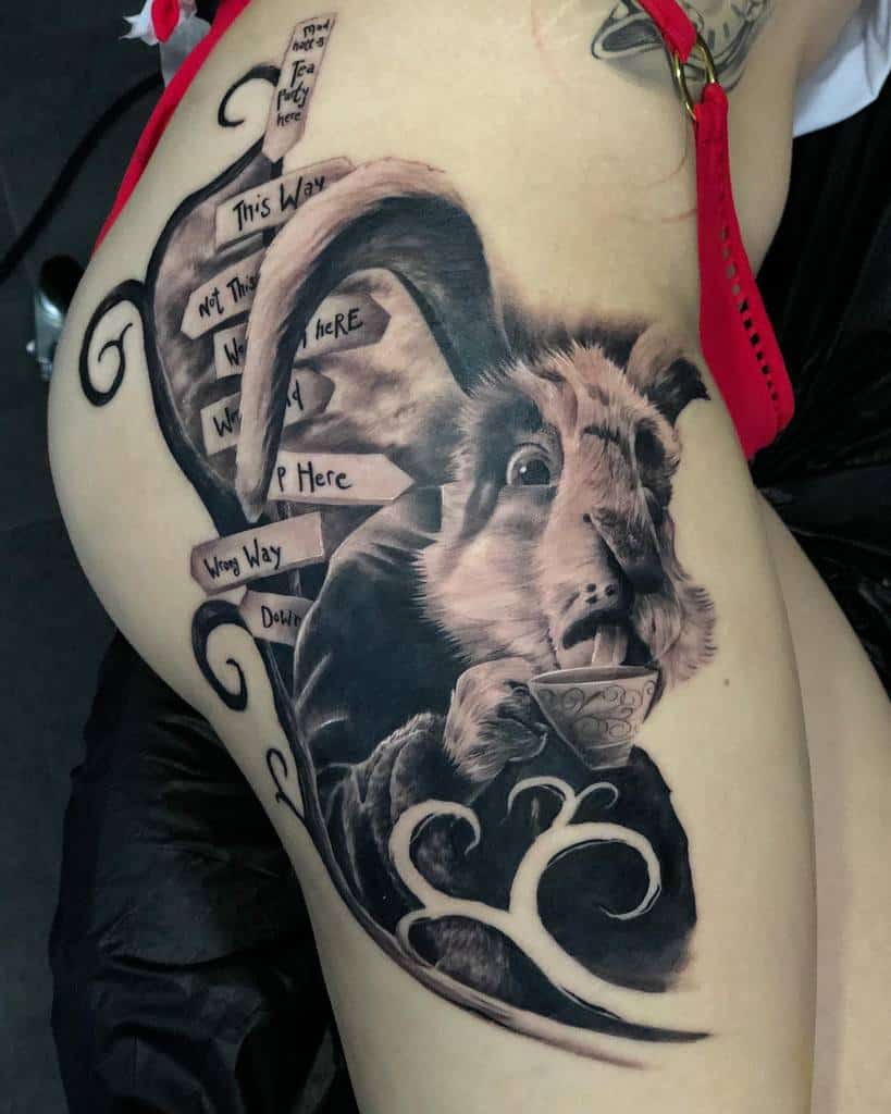 Black and gray tattoo of the White Rabbit from Alice in Wonderland, holding a tea cup, with whimsical signposts around him reading 'This Way,' 'Not This Way,' and 'Wrong Way,'etc.