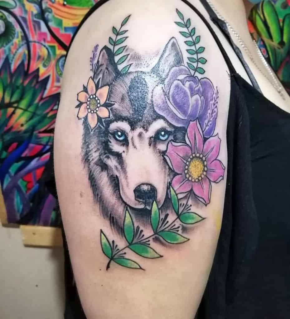 Colorful wolf tattoo with flowers and leaves on a woman's upper arm