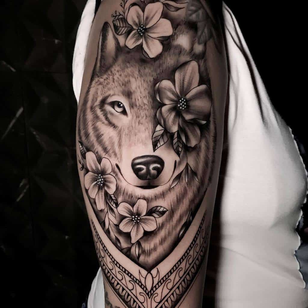 Tattoo of a wolf surrounded by flowers on a woman's arm, showcasing intricate shading and detail