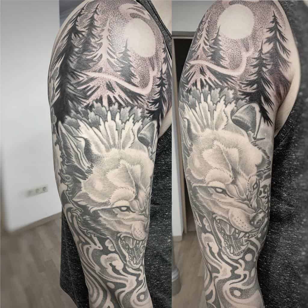 Tattoo of a wolf and forest scene on a person's upper arm in black and gray