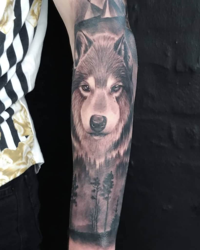 Detailed wolf tattoo on a man's forearm with forest background