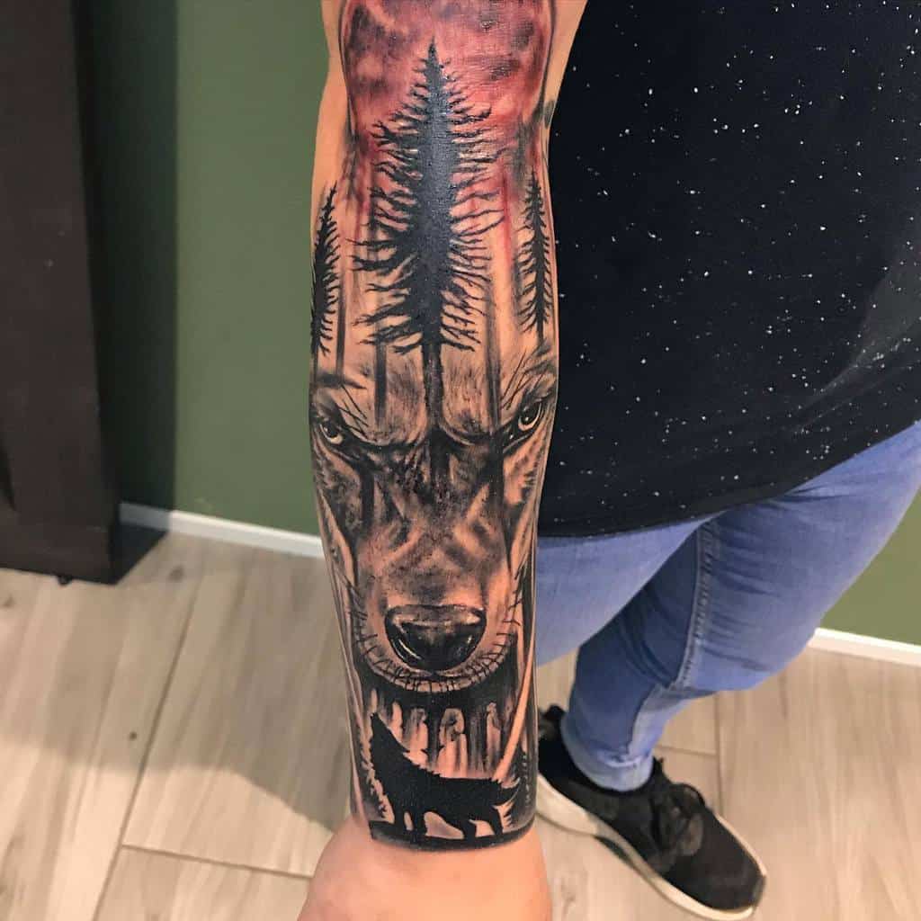 Forearm tattoo of a wolf with forest elements and a silhouette of a howling wolf at the bottom