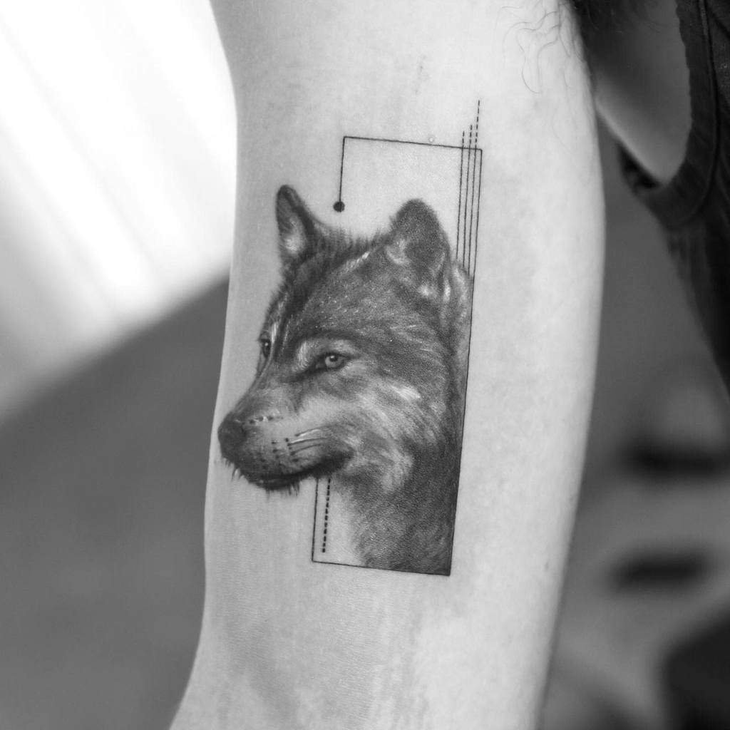 Black and gray wolf tattoo with geometric lines on an upper arm