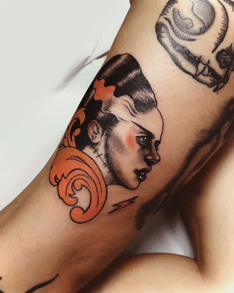 Art Nouveau-inspired tattoo of a woman's face with Bride of Frankenstein elements, bold black shading, and ornate orange swirls