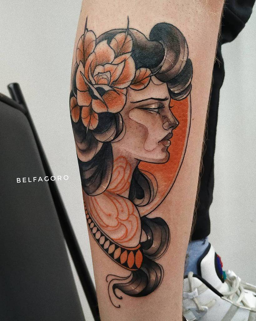Art Nouveau-inspired tattoo of a woman's profile with flowing black hair, orange floral accents, and intricate ornamental details