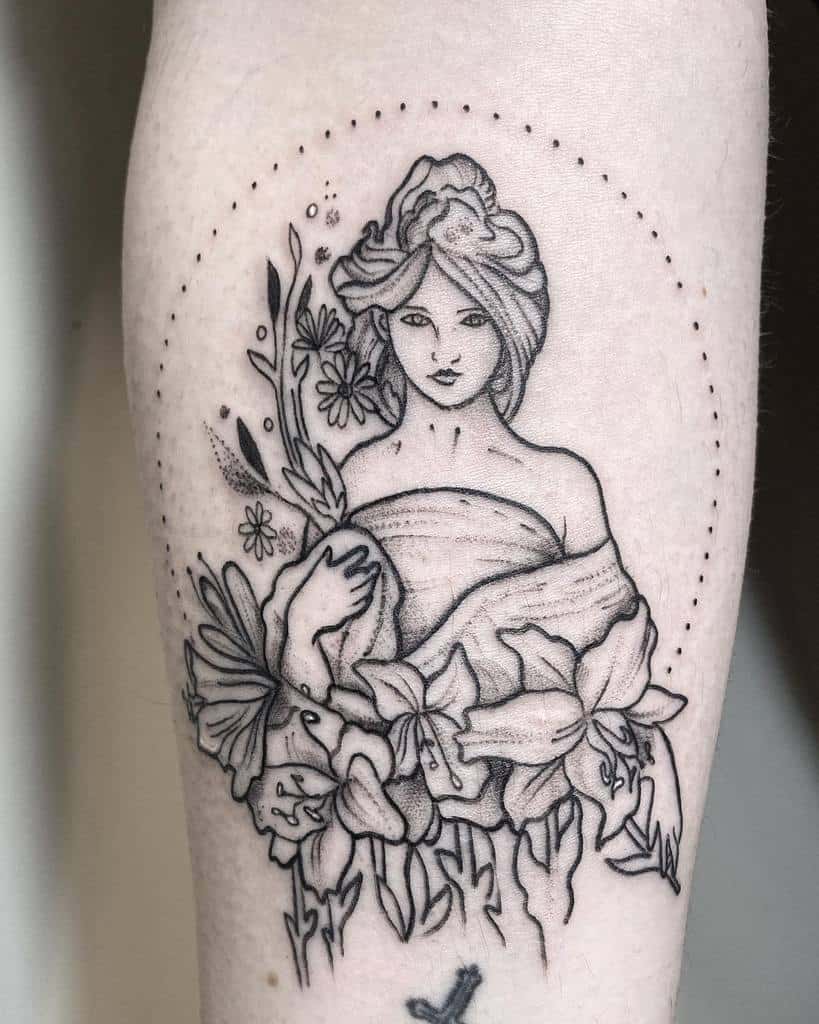 Black and grey Art Nouveau tattoo of a woman with flowing hair, surrounded by lilies and wildflowers, enclosed in a dotted circle