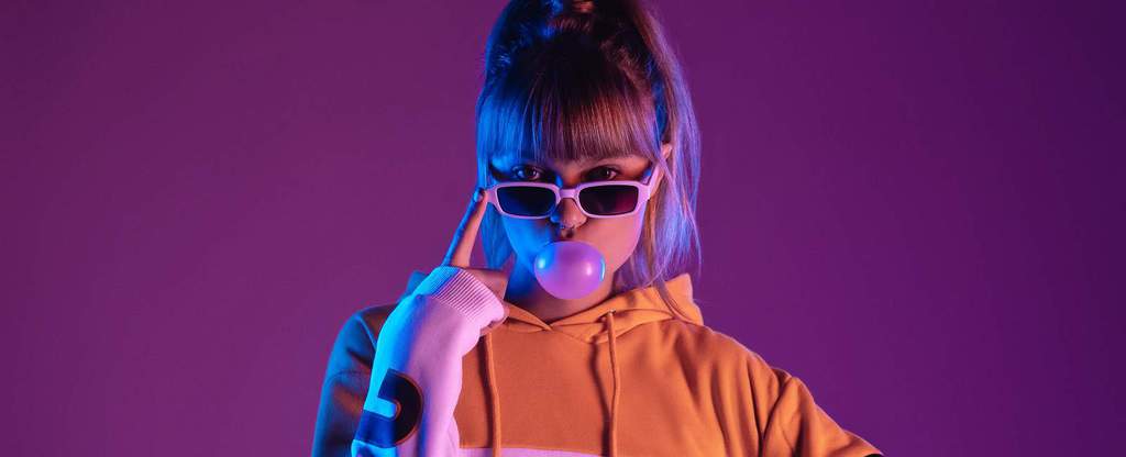 Woman wearing 90s style hoodie and sunglasses blowing bubblegum