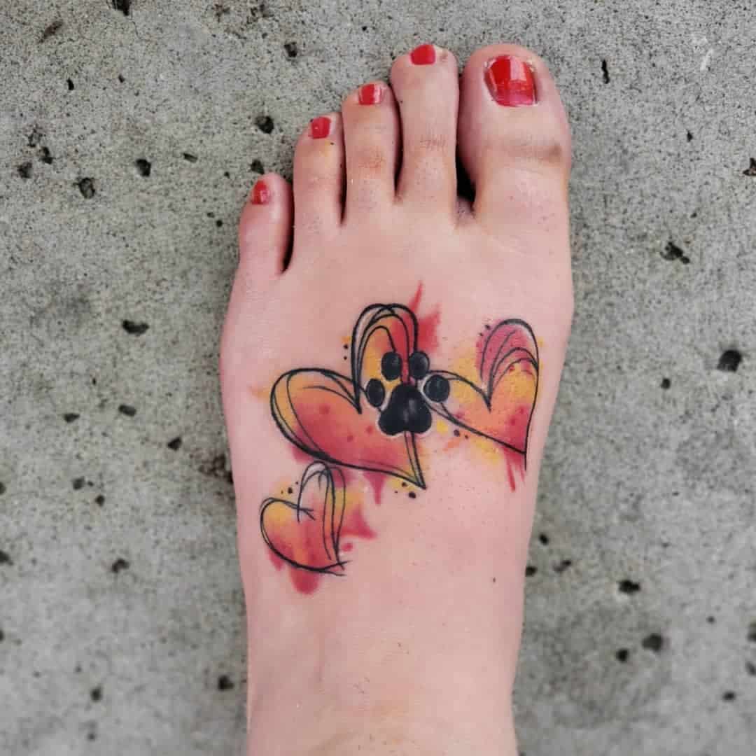 Foot tattoo with three watercolor hearts, one containing a black paw print