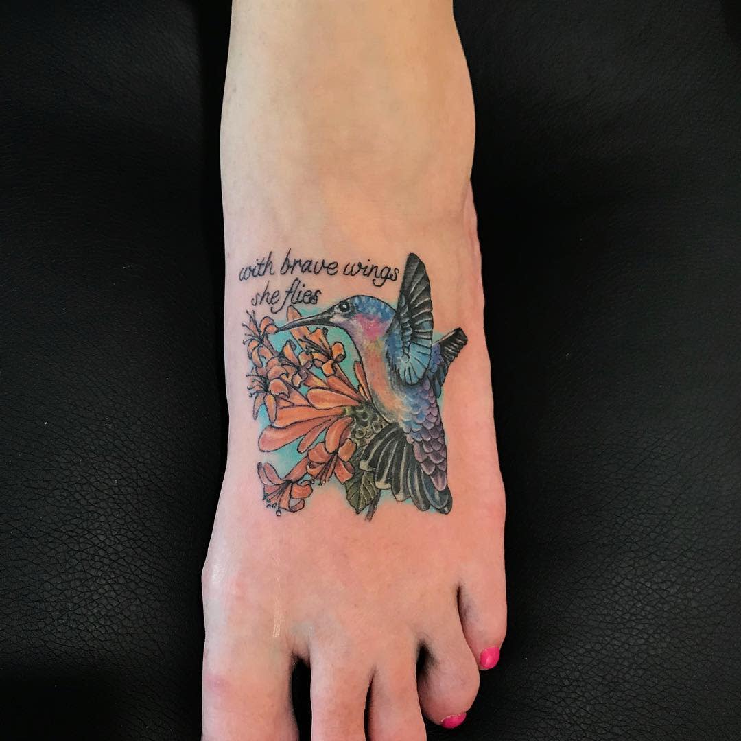 Colorful hummingbird tattoo with the phrase "with brave wings she flies" on a foot