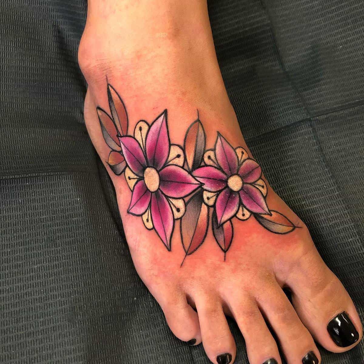 Foot with black nail polish and a tattoo of three pink flowers with green leaves on the top
