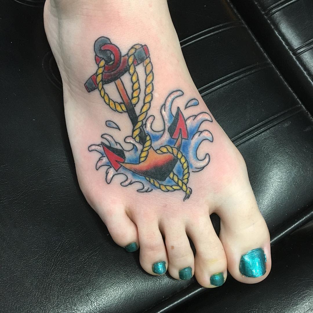 Foot with an anchor tattoo in vibrant colors surrounded by waves