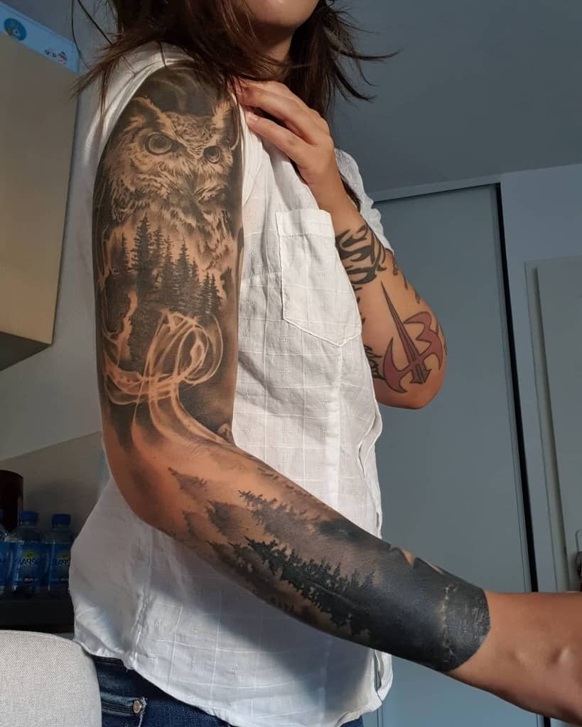 Captivating forest sleeve tattoo for women featuring a majestic owl above a dense woodland scene, with intricate smoke-like patterns flowing gracefully across the design