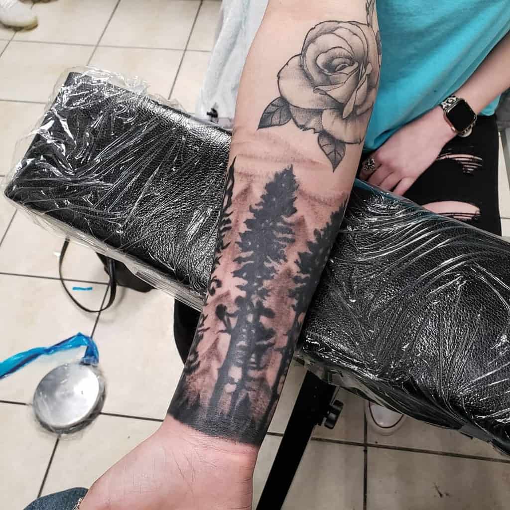 Forearm tattoo of trees and a deer, with a rose above, on an arm