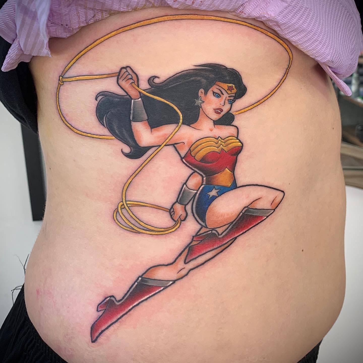 Tattoo of Wonder Woman with a lasso, wearing red and blue outfit, on side torso