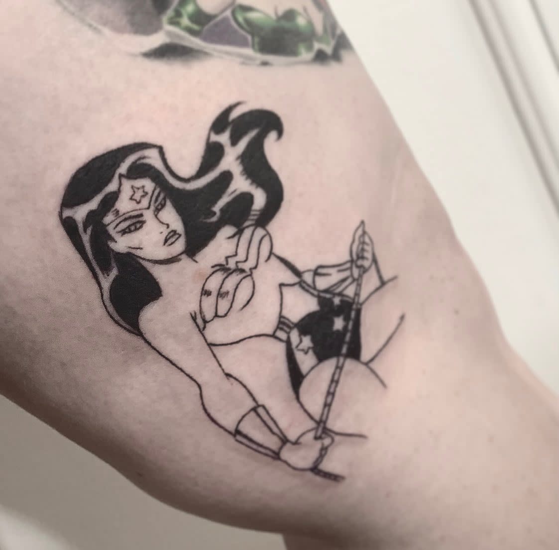 Black and white tattoo of a Wonder Woman with long hair and a star on her forehead, holding a rope