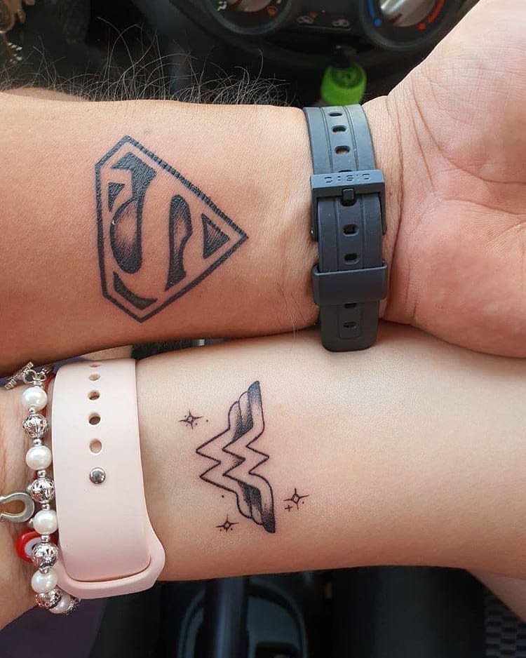 Matching Superman and Wonder Woman wrist tattoos in black ink, with Superman's logo and Wonder Woman's logo adorned with small stars