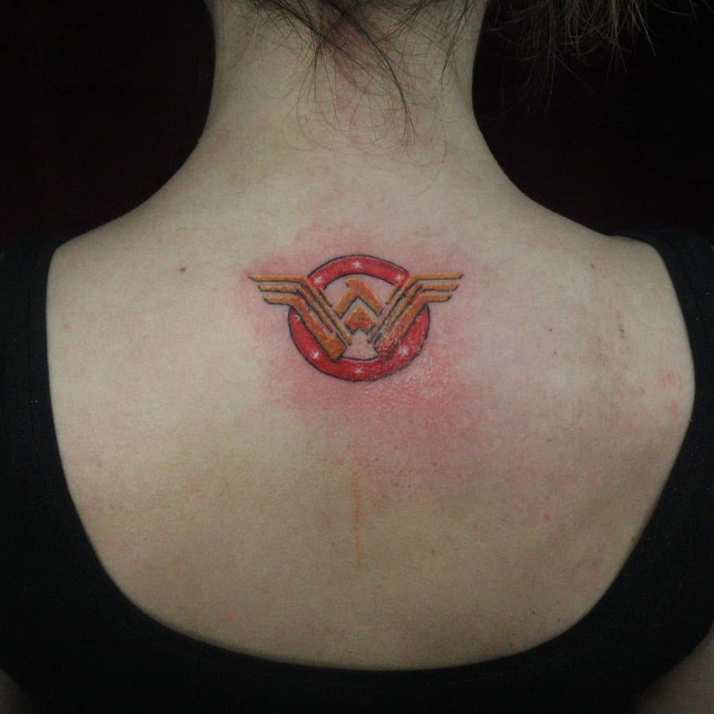 Small Wonder Woman logo tattoo on the upper back, featuring a bold red background with subtle shading