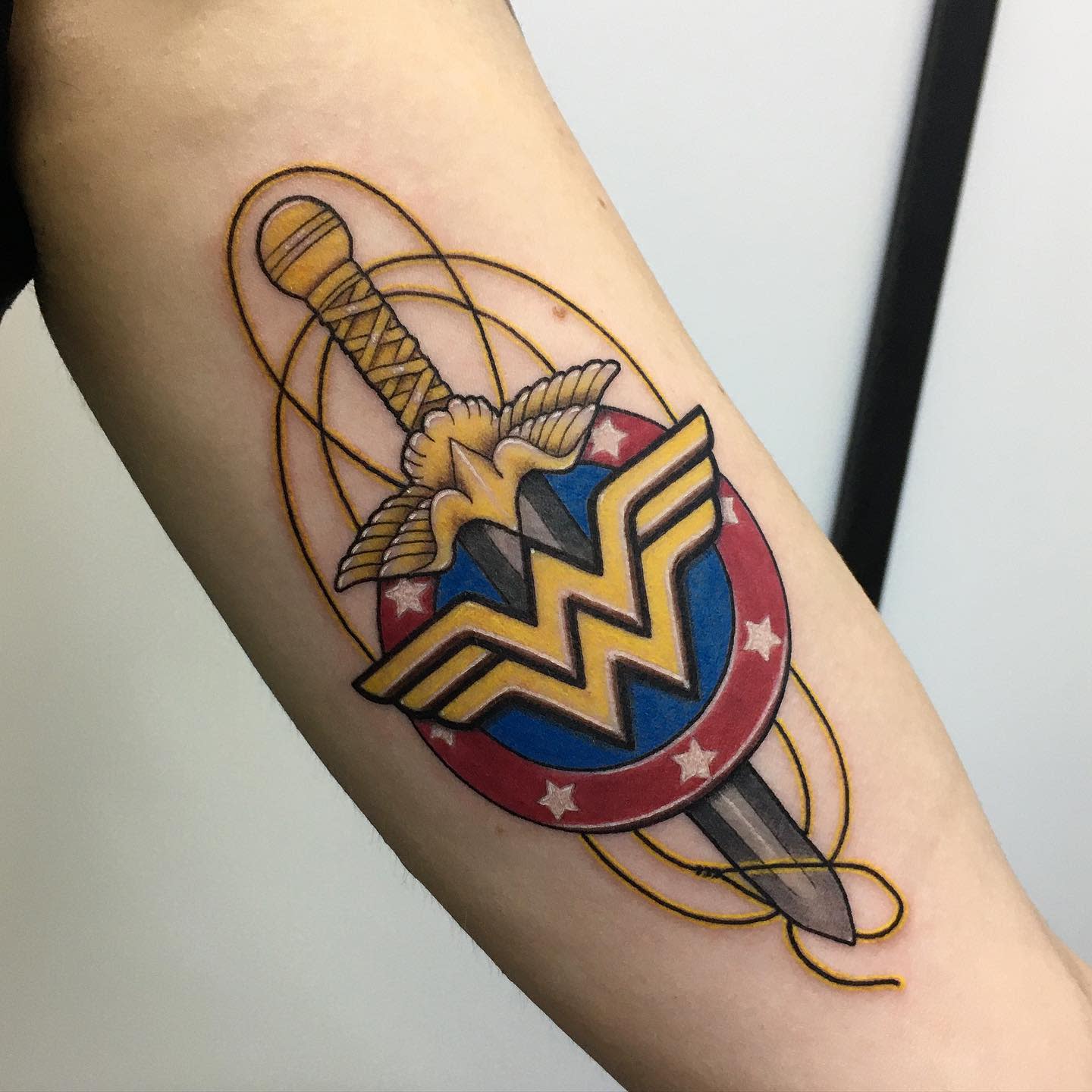 Wonder Woman logo tattoo with a sword and lasso, detailed with vibrant colors and intricate linework