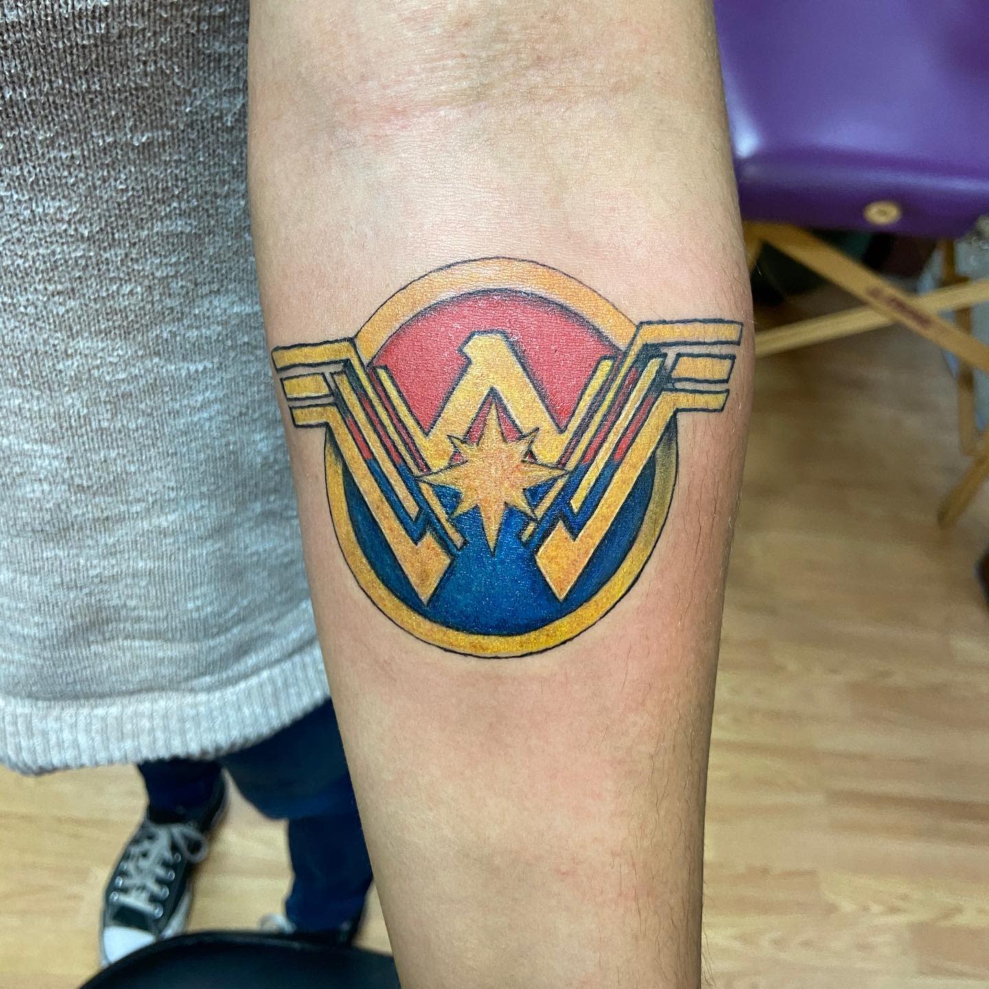 Wonder Woman logo tattoo with a bold circular design, featuring vibrant red, blue, and yellow colors with a central starburst