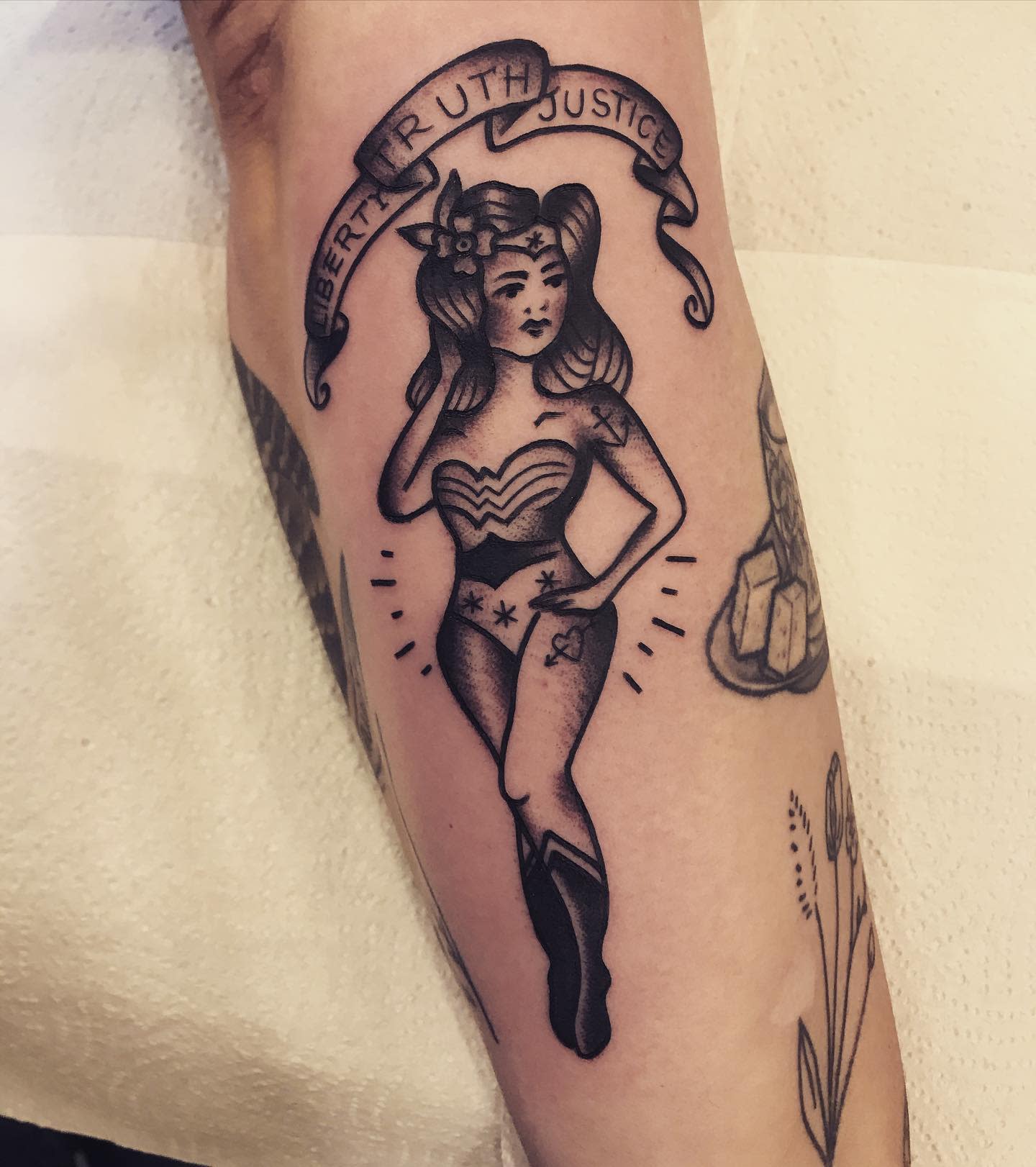Black and gray pin-up style Wonder Woman tattoo, with a banner that reads 'Liberty, Truth, Justice