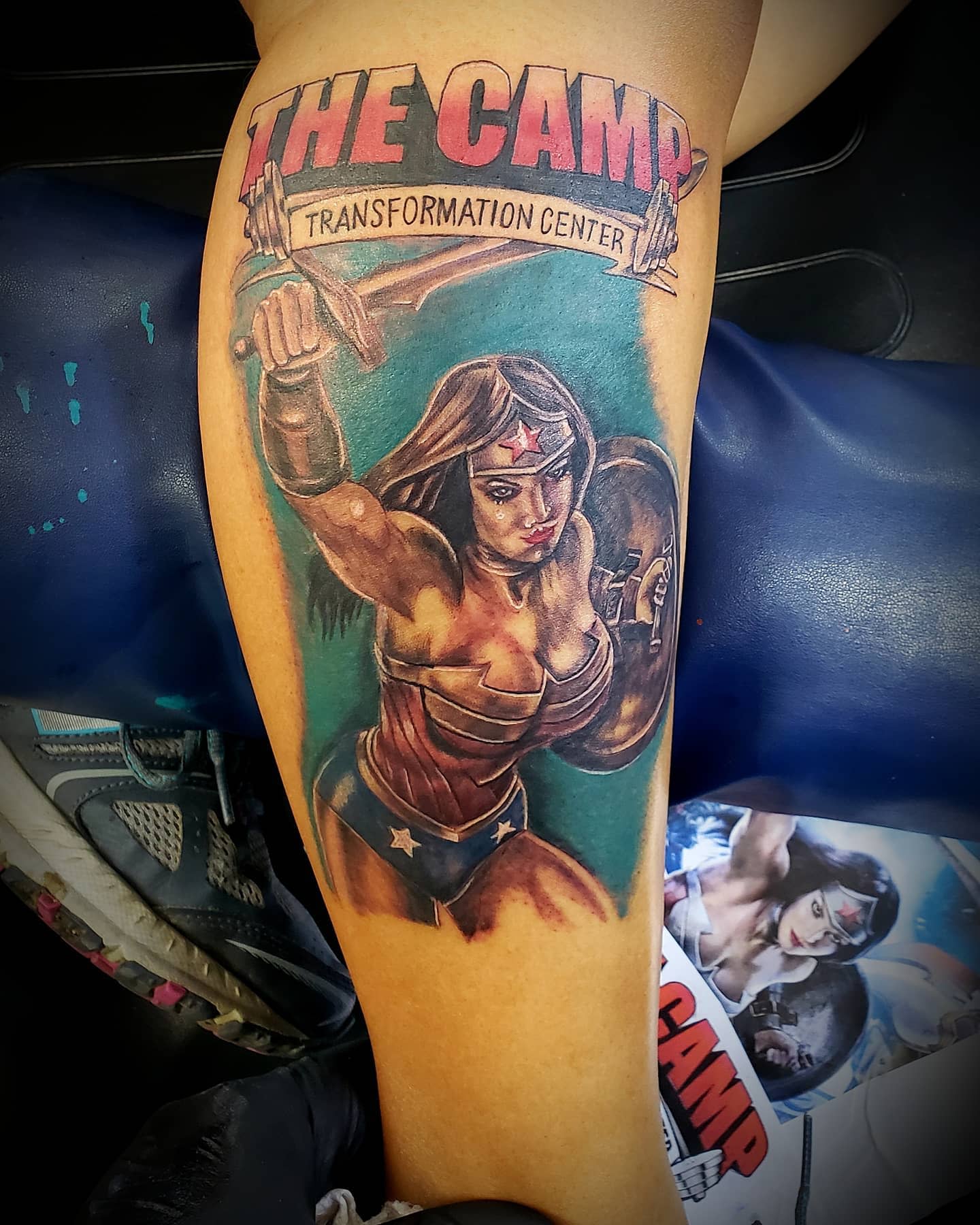 Warrior Wonder Woman tattoo depicting her in a powerful pose, holding a sword and shield, with a banner above that reads 'The Camp Transformation Center'