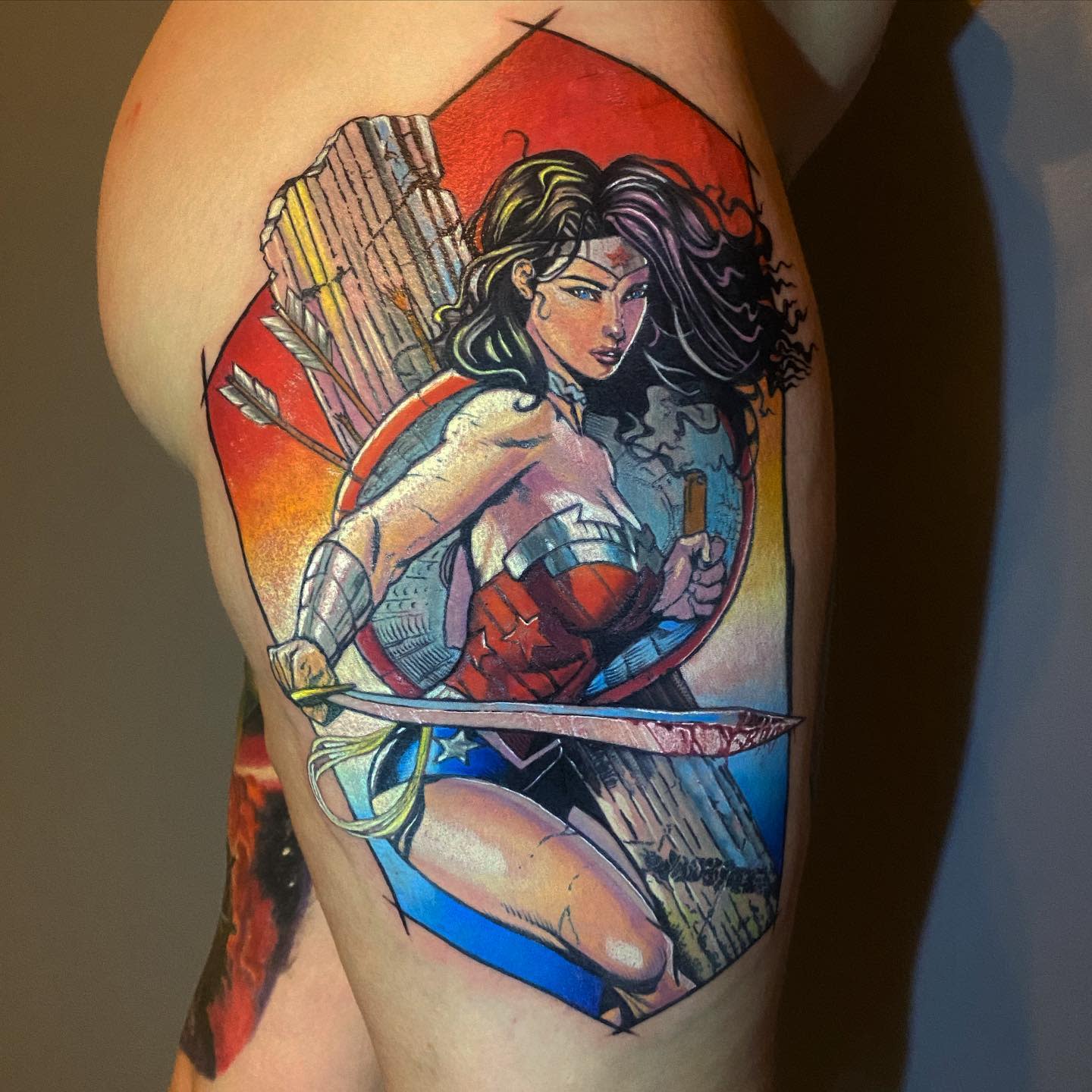 Warrior Wonder Woman tattoo showcasing her in an action pose, armed with a sword, a shield on her back, and a quiver of arrows, against a dynamic background in vibrant colors