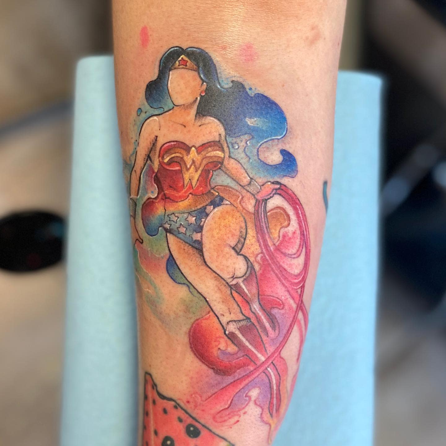 Watercolor-style Wonder Woman tattoo with vibrant colors and flowing lasso, face left blank for emphasis
