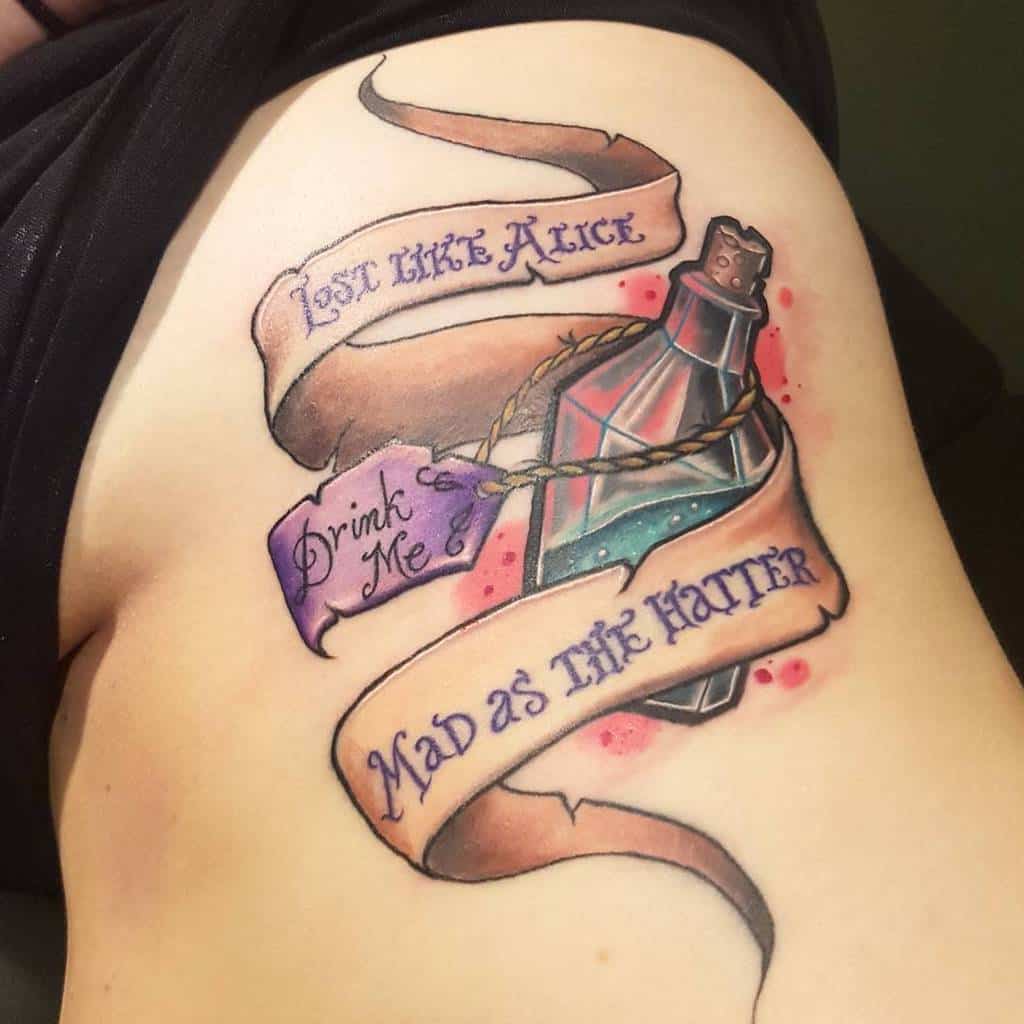 A tattoo featuring a bottle labeled "Drink Me" with banners reading "Lost Like Alice" and "Mad as the Hatter," inspired by Alice in Wonderland