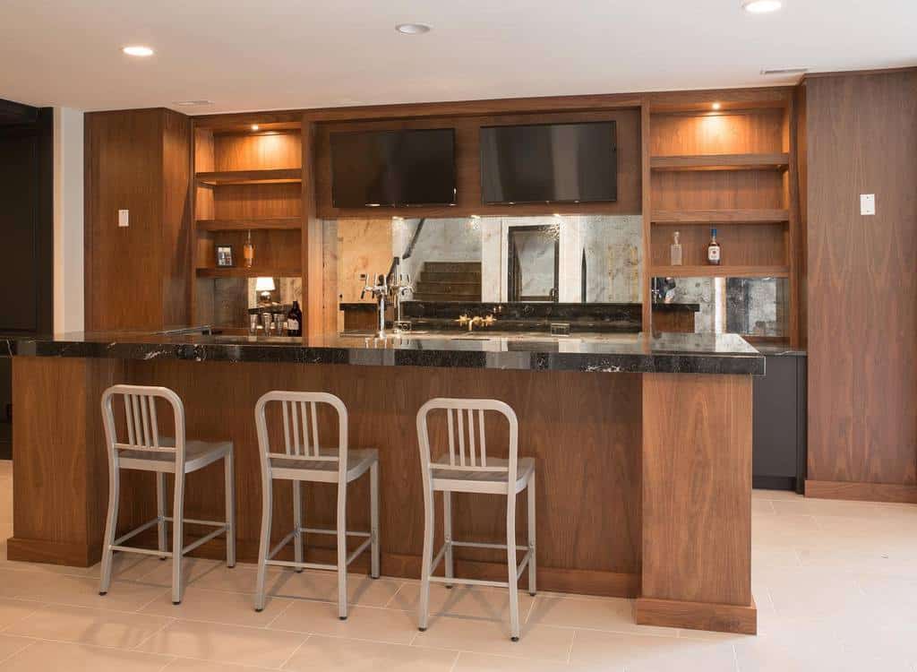Modern wood basement bar with black marble countertop, open shelving, and metal bar stools.