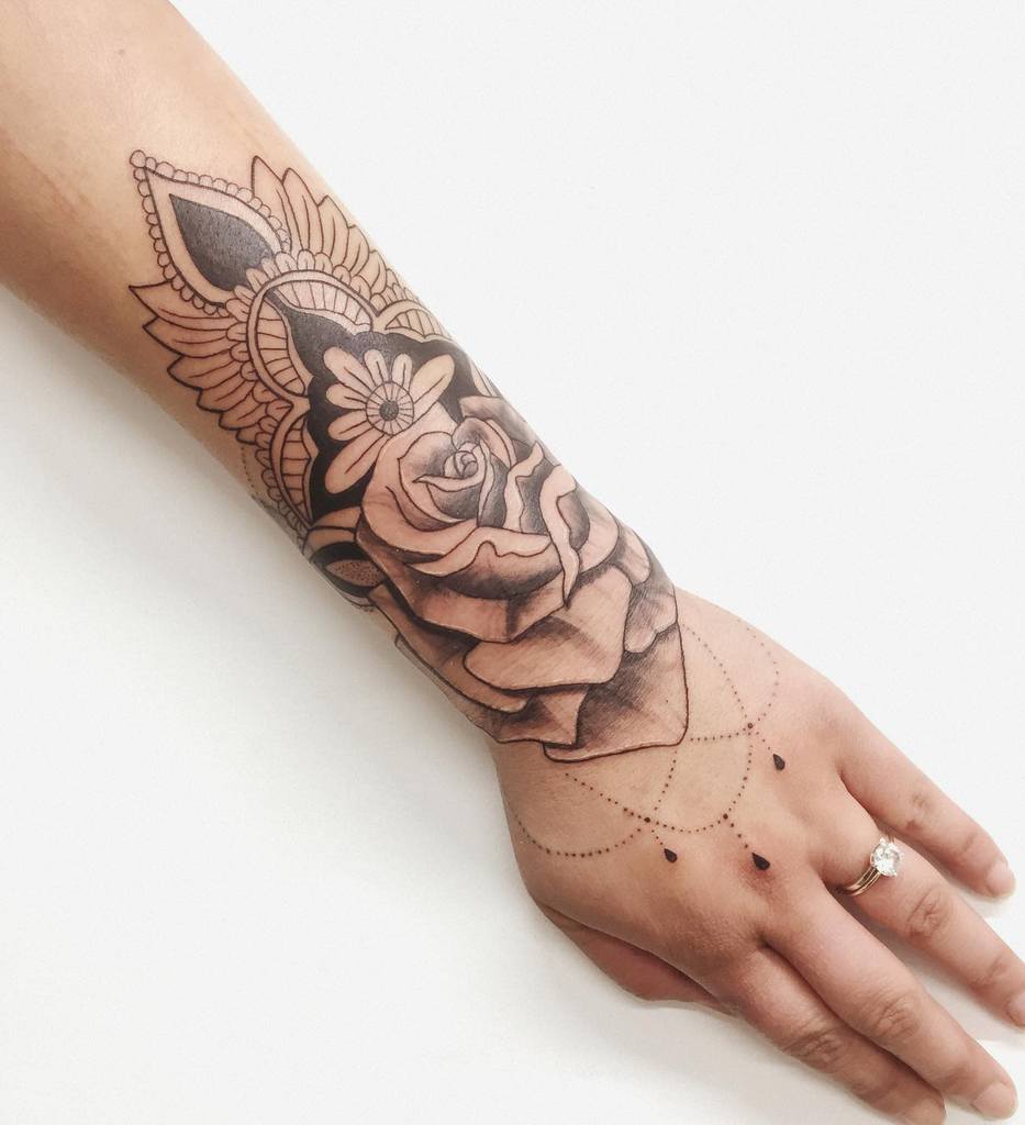 Chandelier-style forearm tattoo featuring a detailed rose, ornamental mandala patterns, delicate beaded chains, and teardrop accents