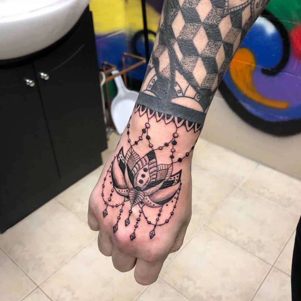 Chandelier-style hand tattoo featuring a detailed lotus flower, beaded chains, diamond-shaped crystals, and ornamental wristband patterns