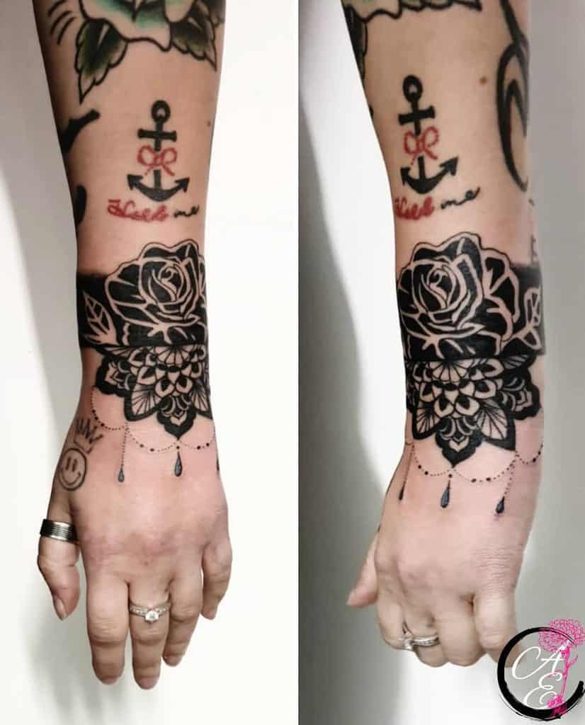 Chandelier-style wrist tattoo featuring a bold black rose, mandala patterns, delicate beaded chains, teardrop accents, and an anchor tattoo above