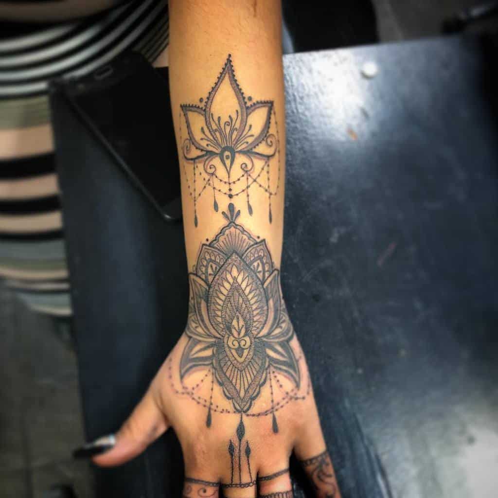 Chandelier-style tattoo featuring two distinct mandala designs on the wrist and hand, with intricate floral patterns, beaded chains, and teardrop accents