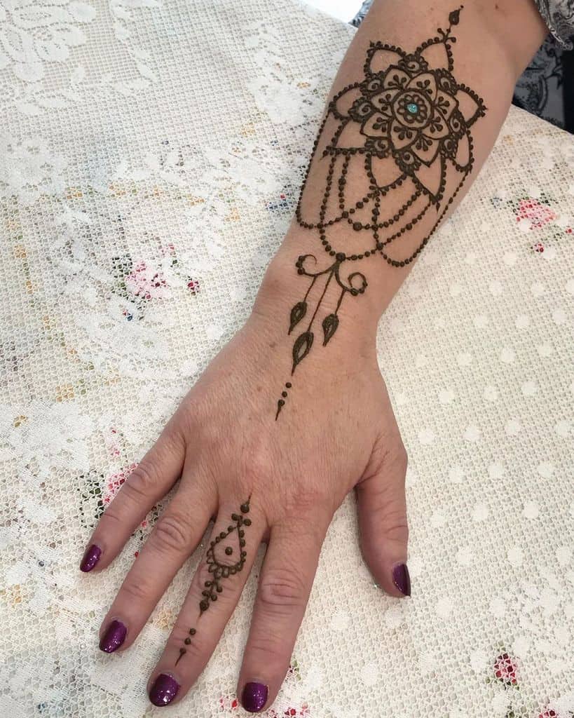 Intricate chandelier-style henna design on hand and wrist, featuring a floral mandala, beaded chains, and delicate leaf-shaped details