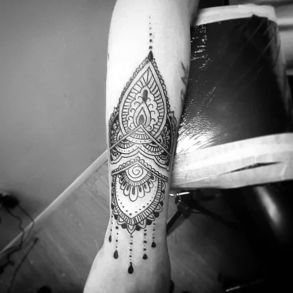 Chandelier-style forearm tattoo featuring an intricate mandala design, ornamental patterns, delicate beaded chains, and teardrop accents